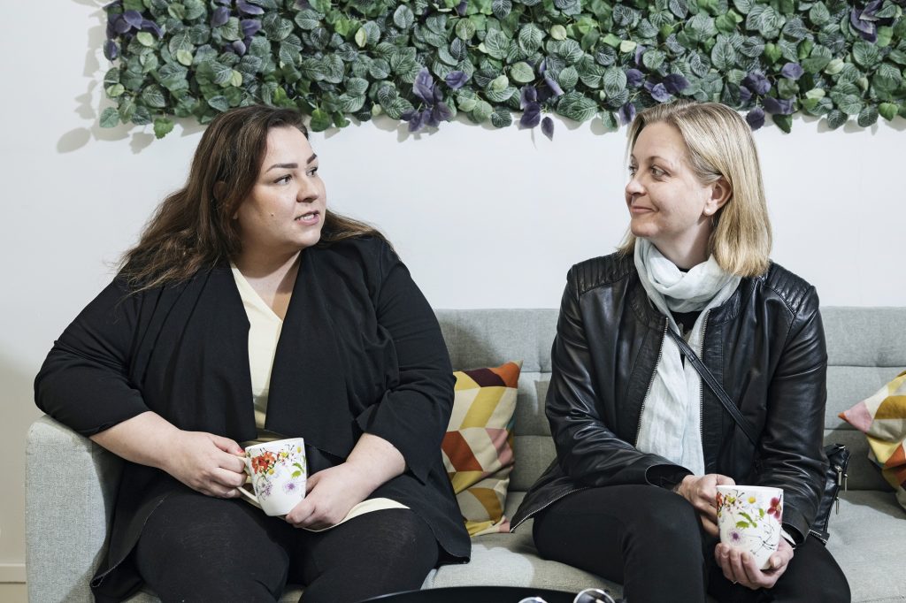 Two women sitting on the sofa with coffee cups in their hands.